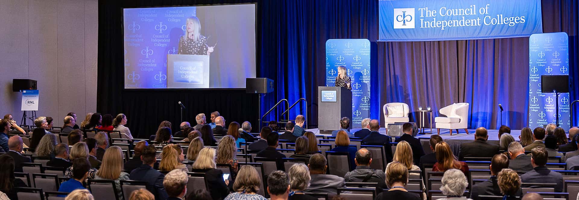 Marjorie Hass speaking on stage from podium in front of seated Institute participants